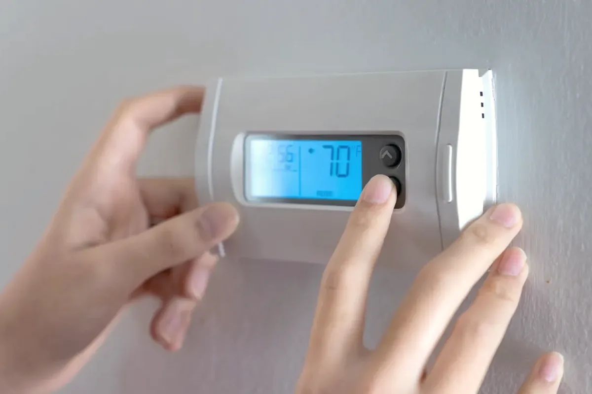 Hands adjusting a digital wall thermostat